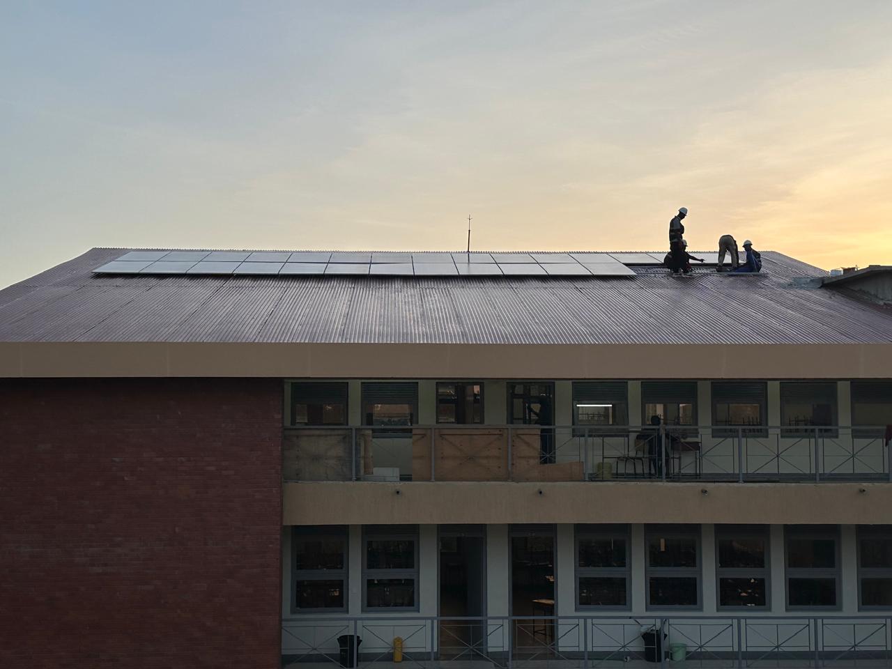 Technicians installing solar panels on a building roof at sunset